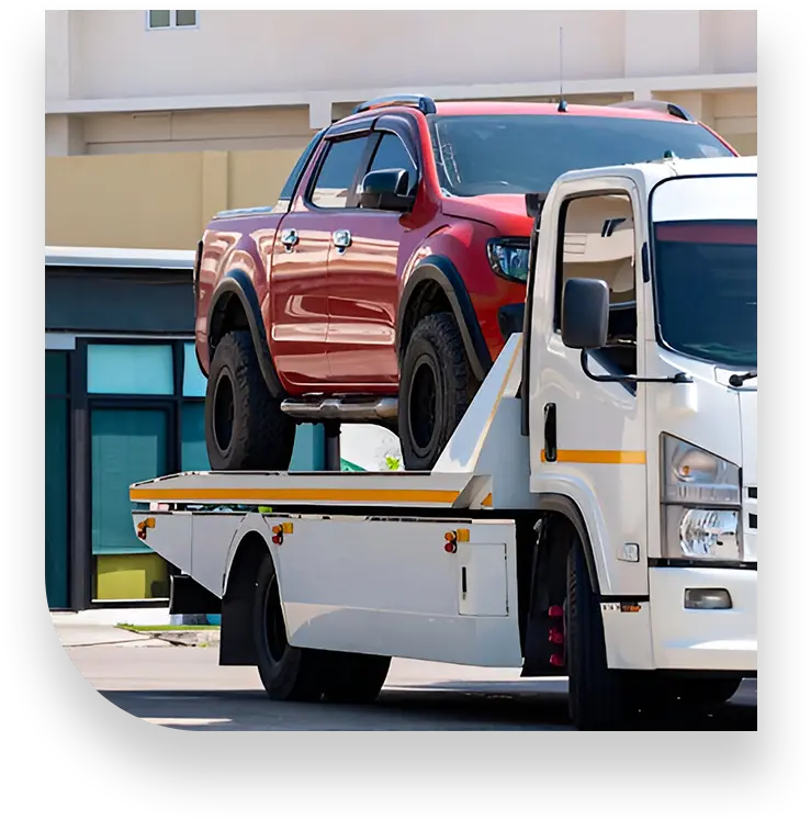 A red pickup truck is being loaded onto a white tow truck on a sunny day, with a modern building in the background.