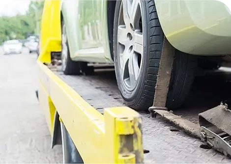 A close-up of a car being loaded onto a yellow tow truck, highlighting the tire and ramp on a paved street.