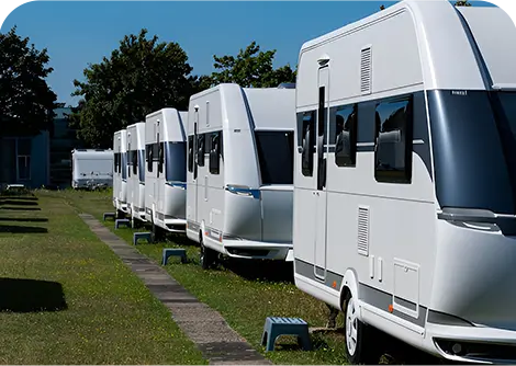 A row of white caravans parked on a grassy area, with a clear blue sky in the background.