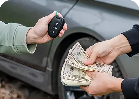 A person hands over car keys while another person exchanges cash, both standing near a parked car.