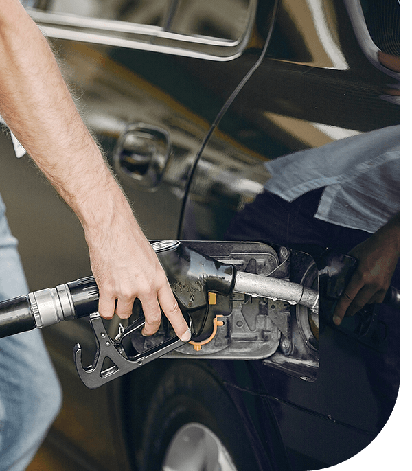 A person refuels a car at a gas station, holding a fuel nozzle and preparing to pump gas into the vehicle's tank.