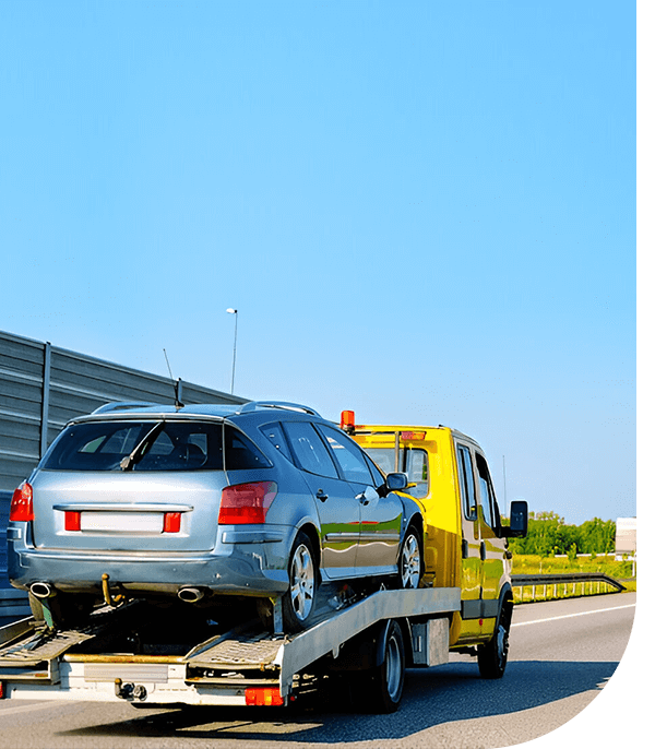 A yellow tow truck transporting a silver car on a flatbed along a sunny highway with clear blue skies.