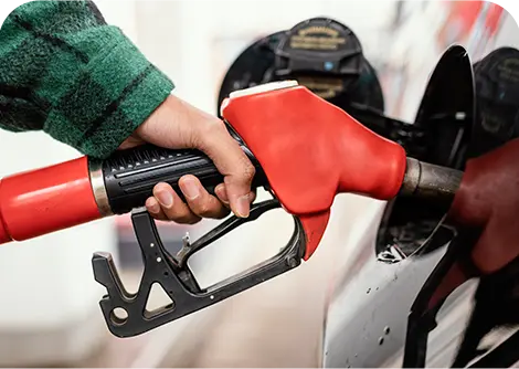 A hand holding a red gasoline nozzle at a fuel pump, inserting it into a vehicle's gas tank.